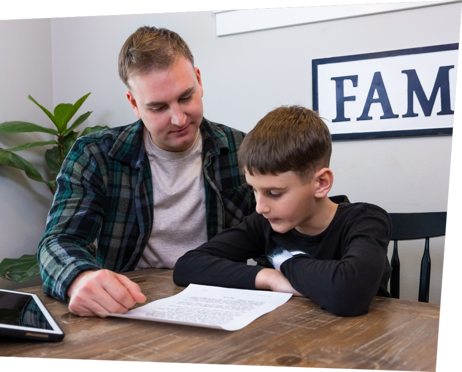 Father going over a reading lesson with his son at a kitchen table.